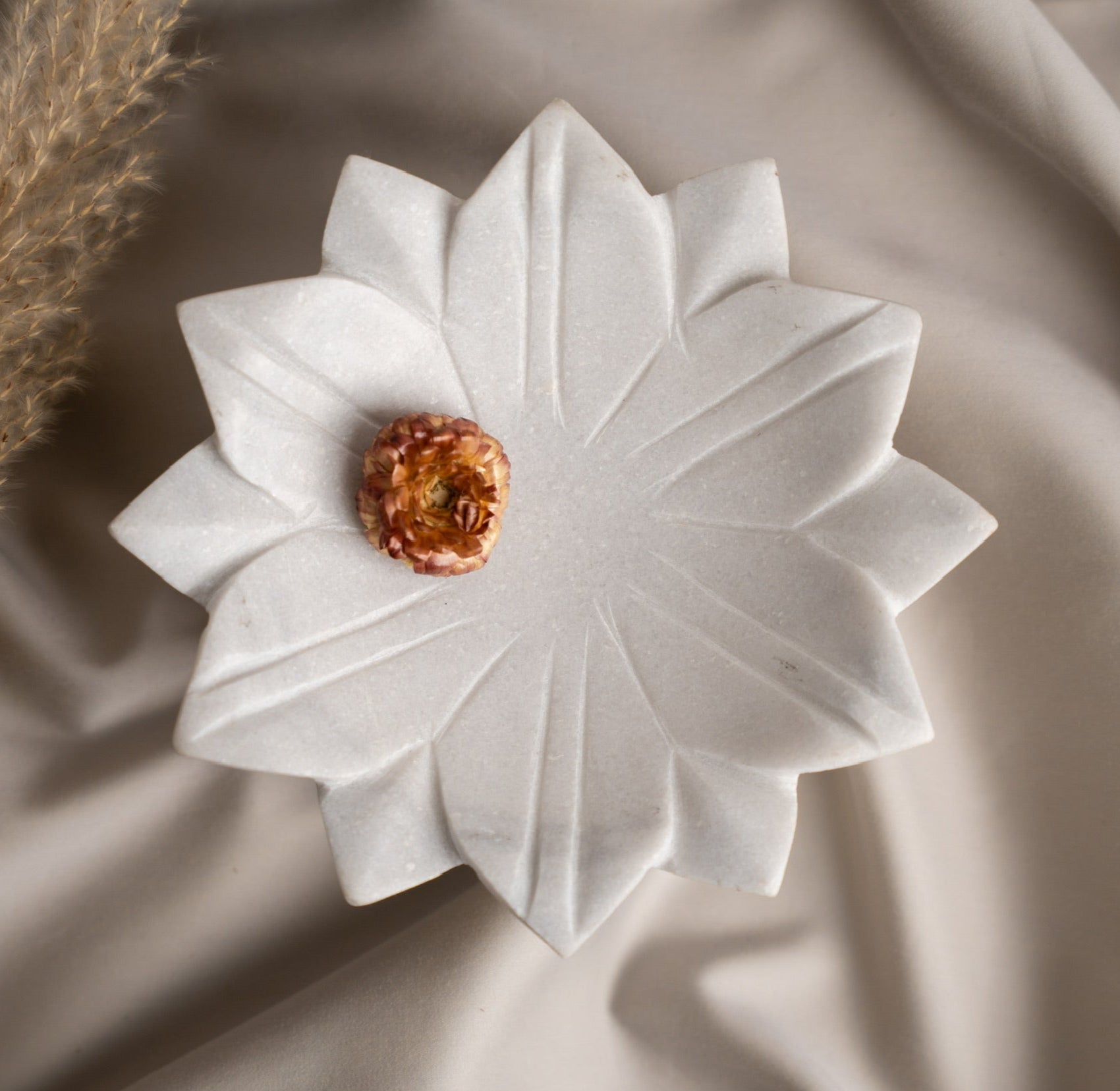 White flower-shaped Marble Urli with a Flower on a beige fabric background. Luxury Gifting